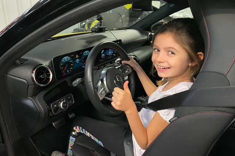 Une enfant souriante au volant d'une Mercedes, ceinture bouclée, lors d'un stage de pilotage enfant