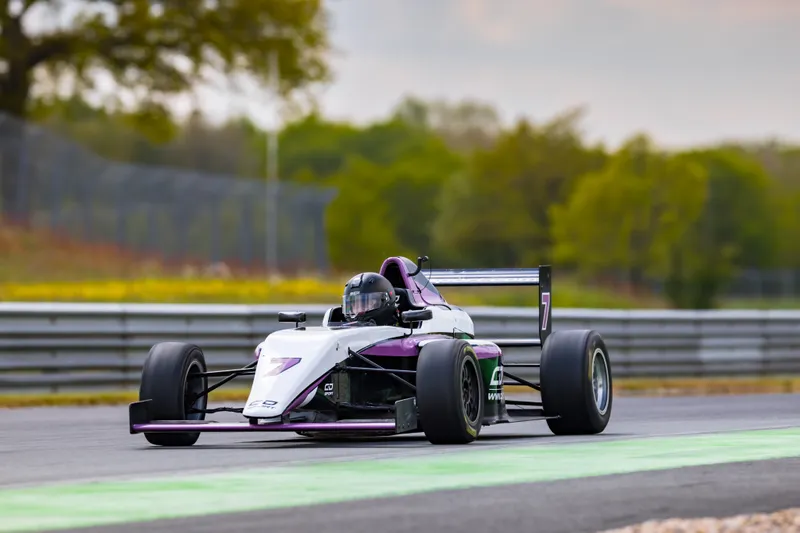 Une monoplace blanche et violette en piste, pilote casqué au volant