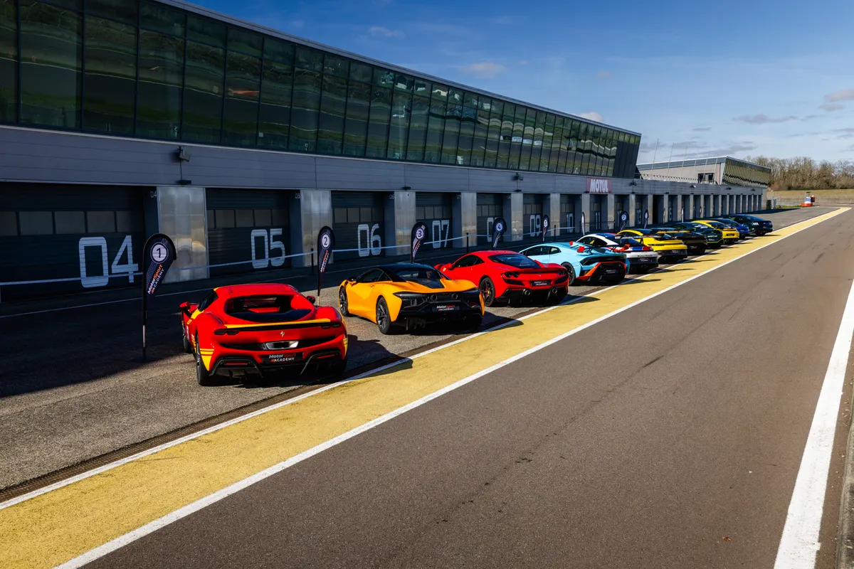 Voitures de sport alignées devant les stands numérotés, sous les oriflammes Motorsport Academy